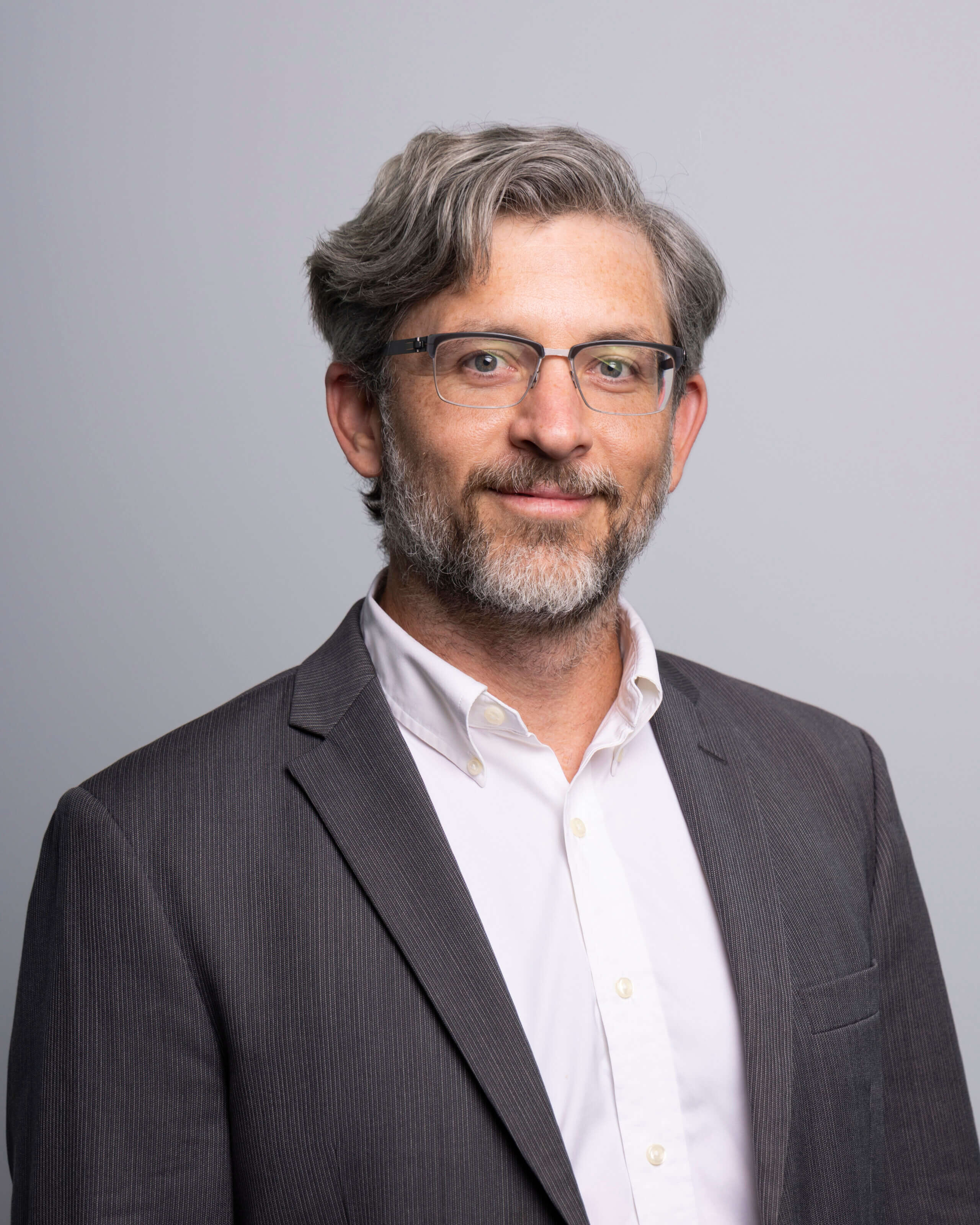 Gabriel Cofield – RNGD executive headshot of Lloyd Schoen, wearing a grey suit and white shirt, posed with a professional expression against a gray background.