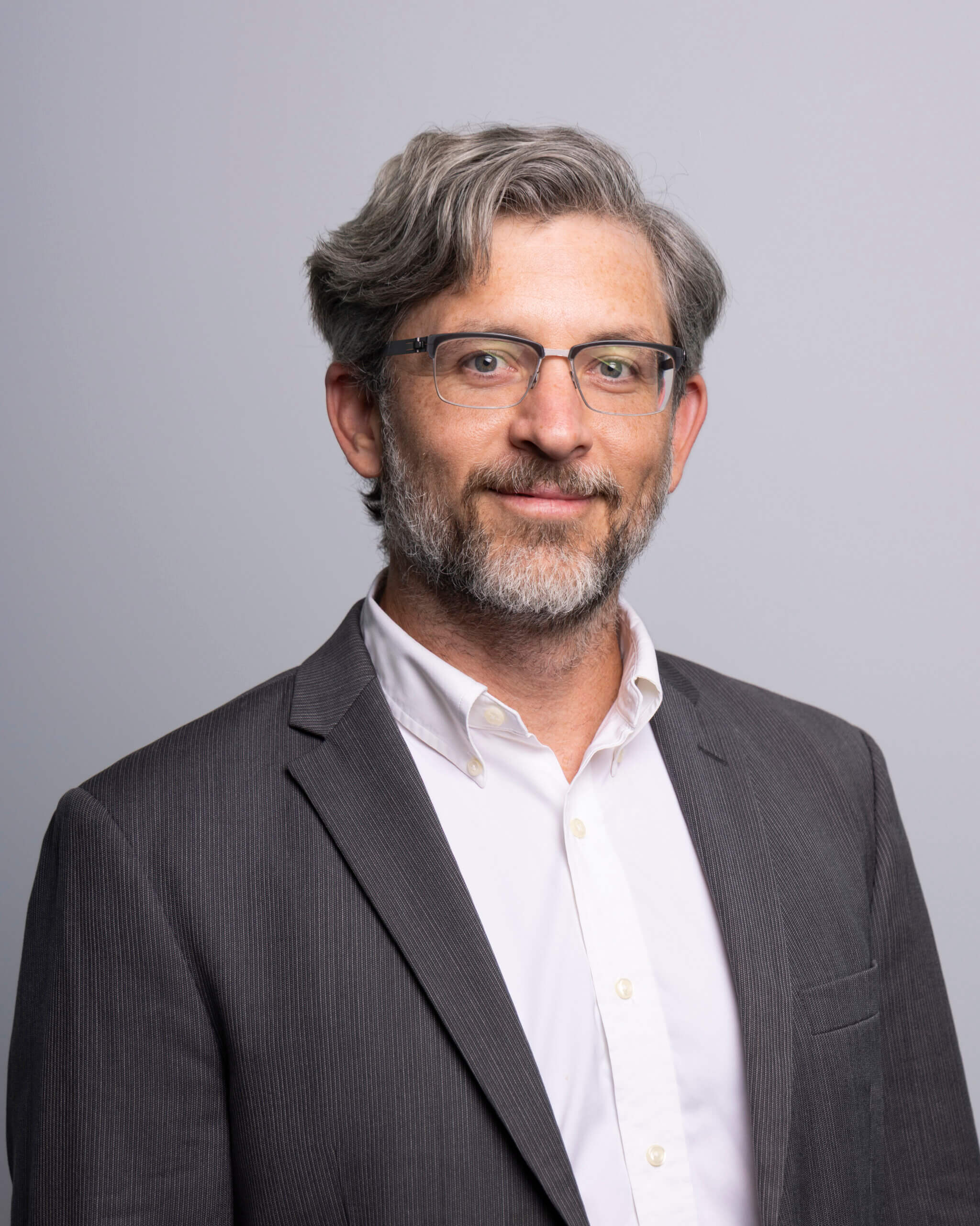 Gabriel Cofield – RNGD executive headshot of Lloyd Schoen, wearing a grey suit and white shirt, posed with a professional expression against a gray background.