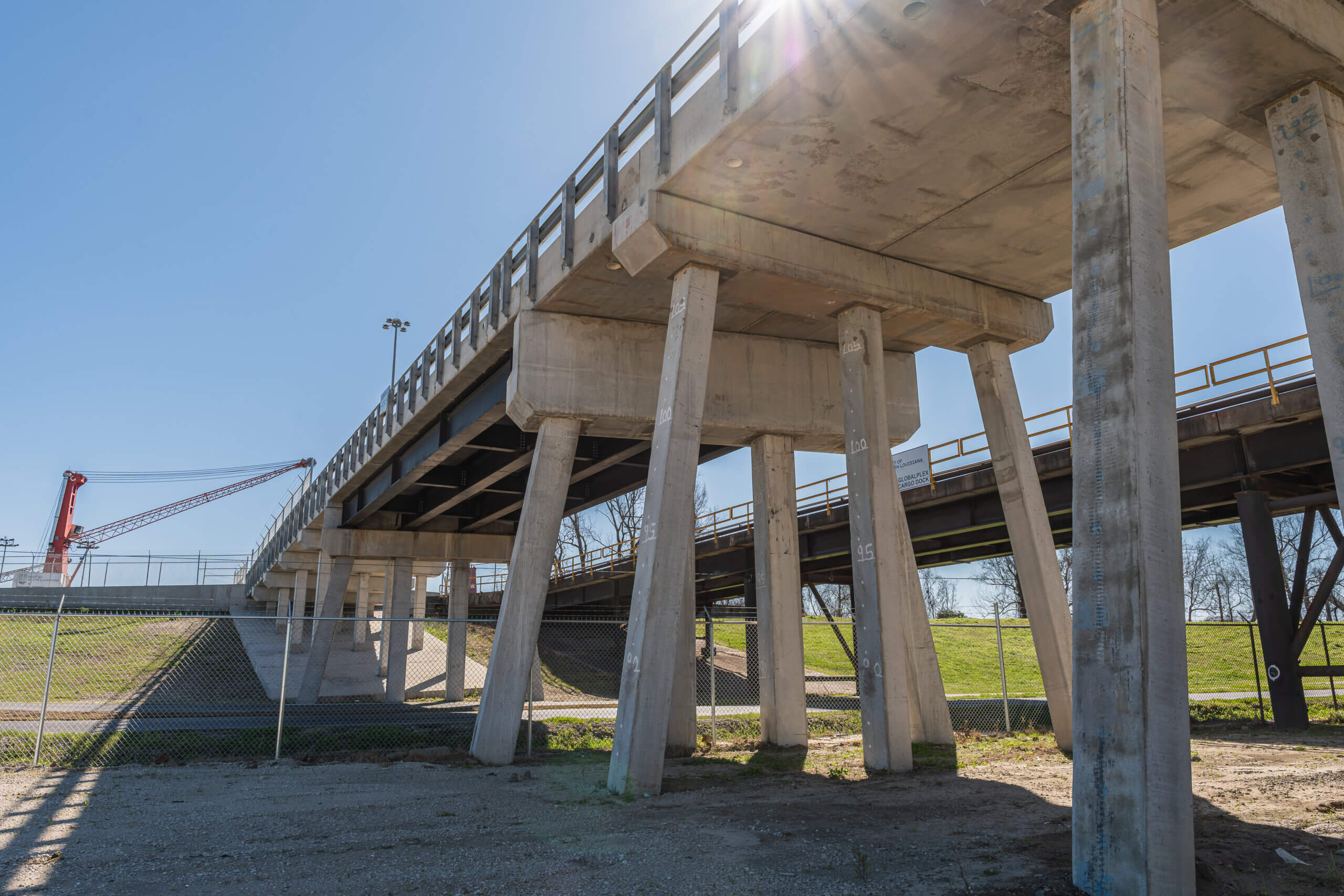 Low-angle view underneath the completed Globalplex Access Bridge showing precast concrete pilings, bent caps, and bridge deck in St. John the Baptist Parish Louisiana