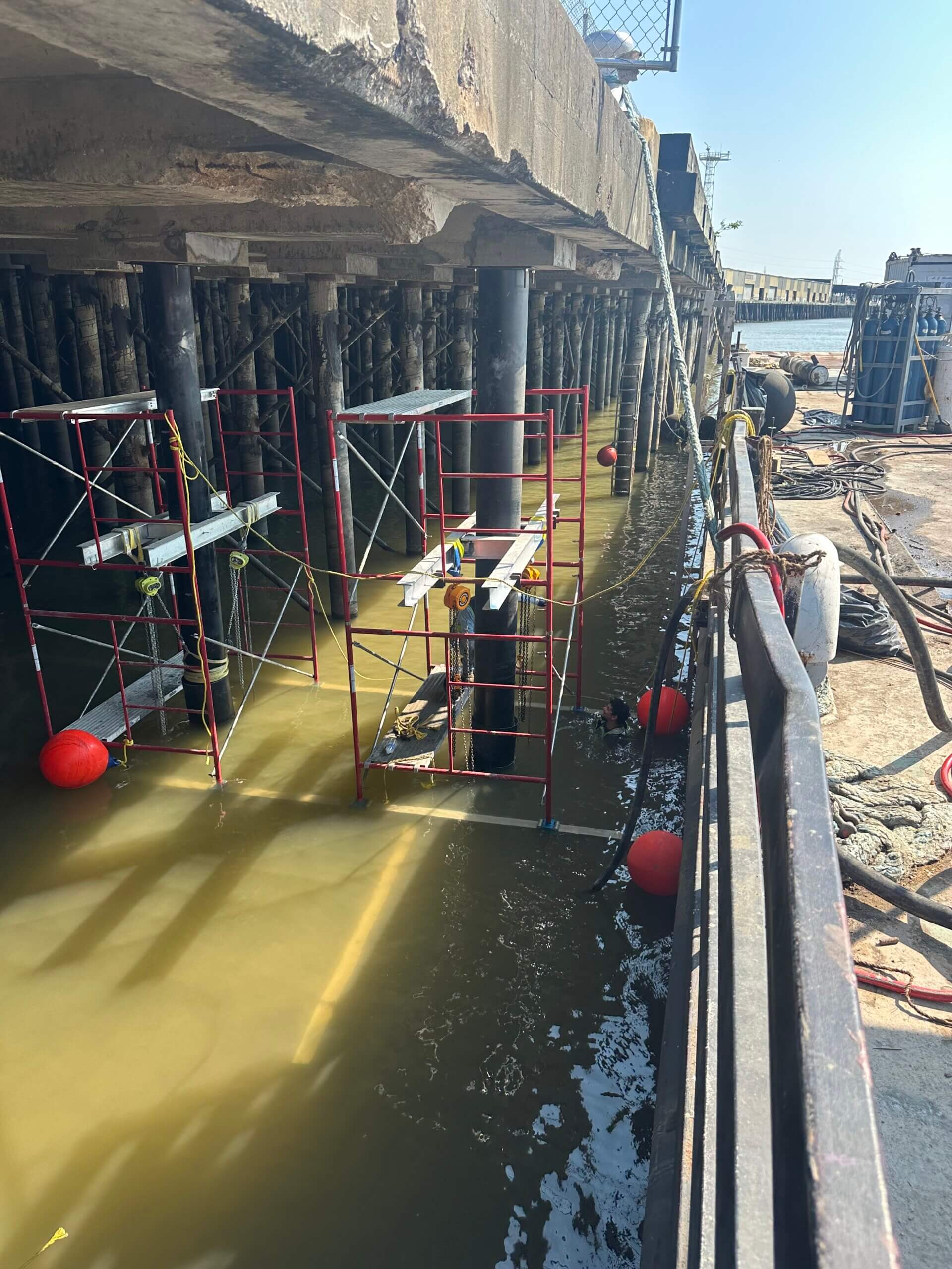 Construction crews and divers working from scaffolding beneath Governor Nichols Wharf to install sleeved pile assemblies.