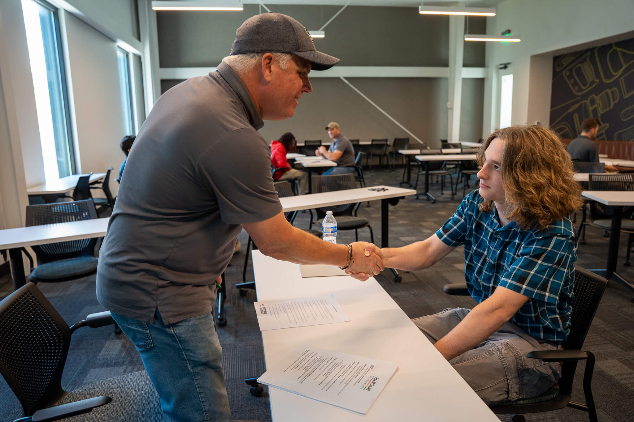 An RNGD team member shakes hands with a student during a career mentorship and networking event inside a classroom setting.