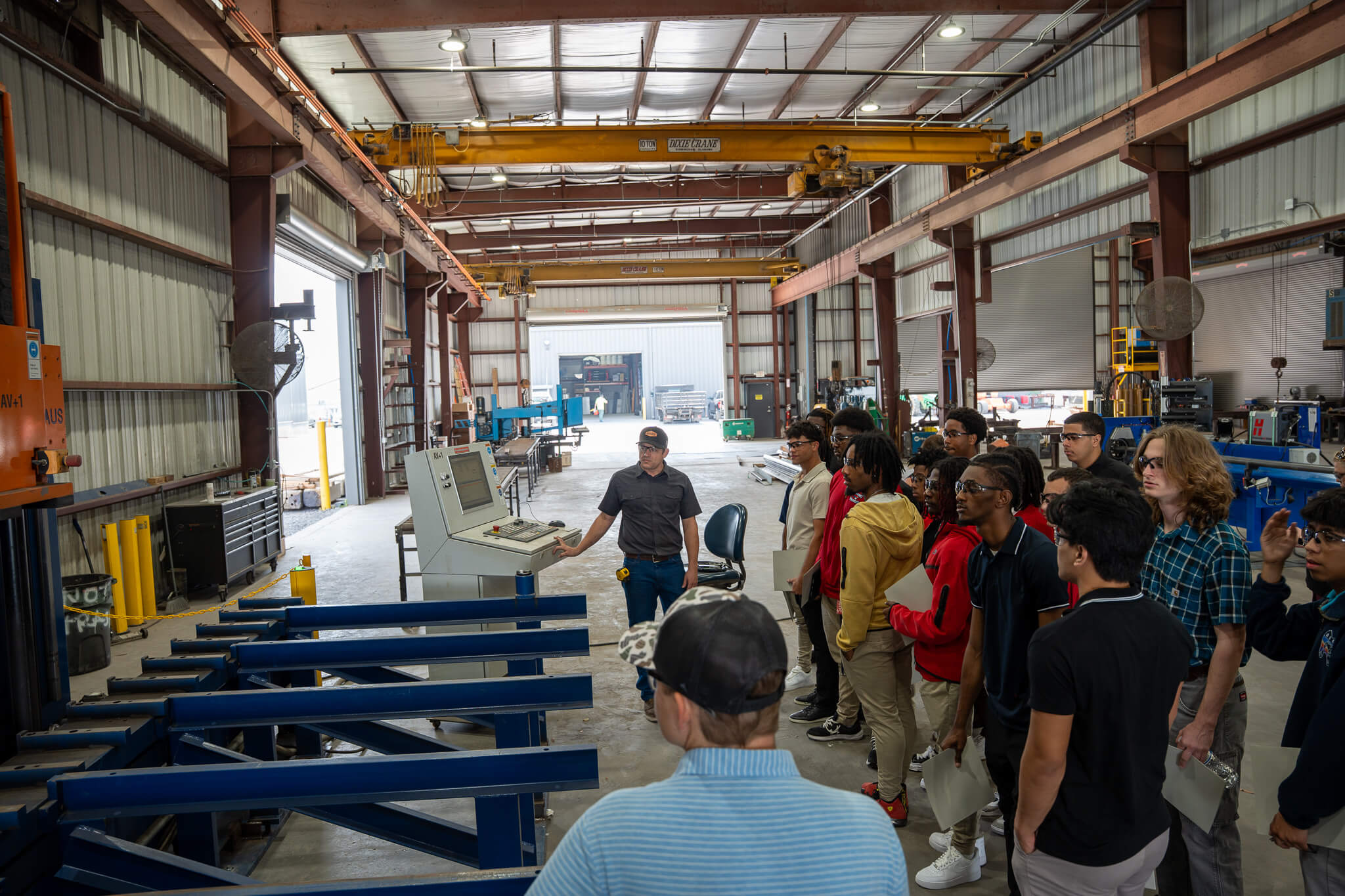 A group of students tours RNGD’s steel fabrication facility while a team member demonstrates industrial equipment and manufacturing operations.