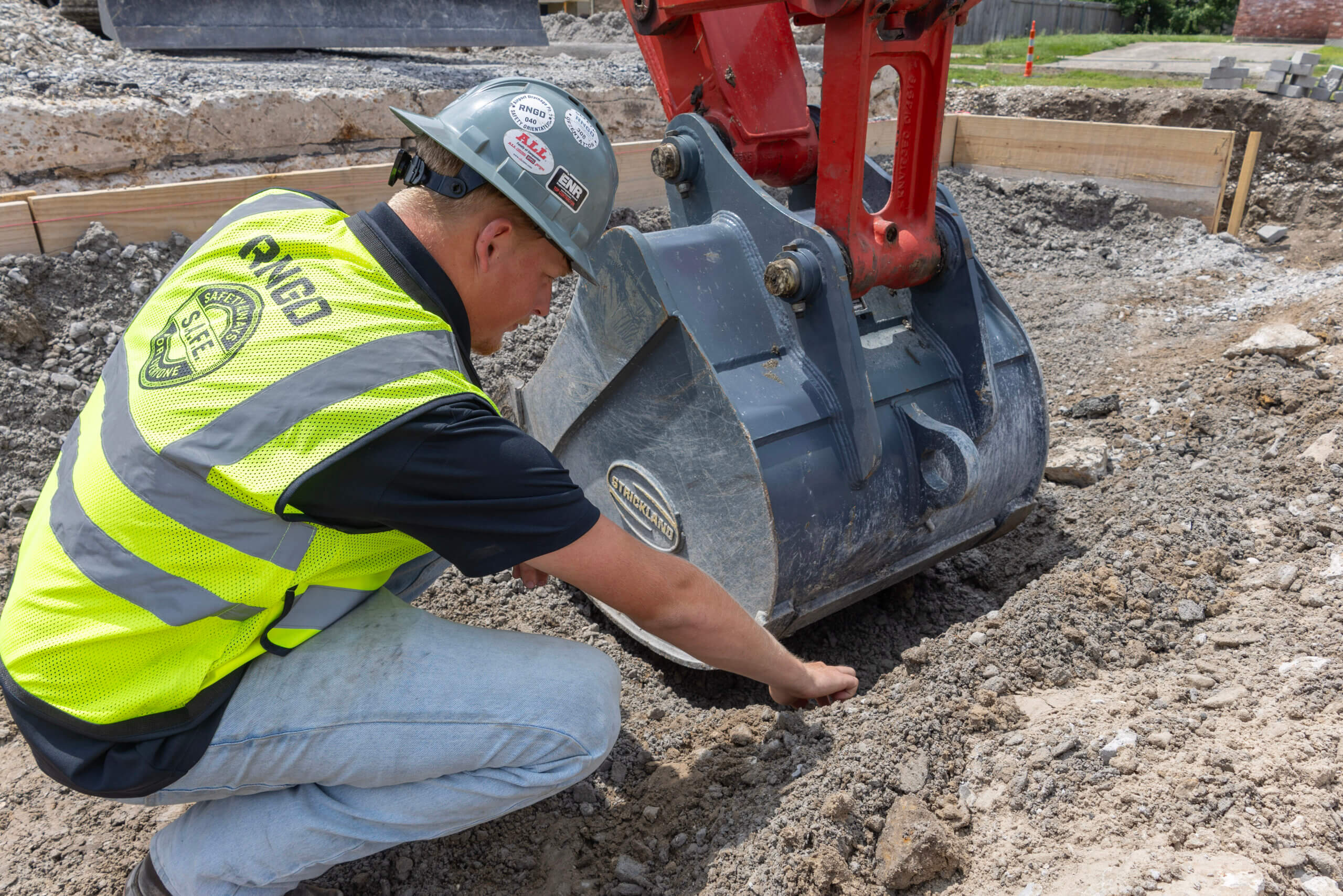 RNGD Project Engineer Makade Penton inspects excavation conditions beside heavy equipment on an active construction site while wearing PPE.