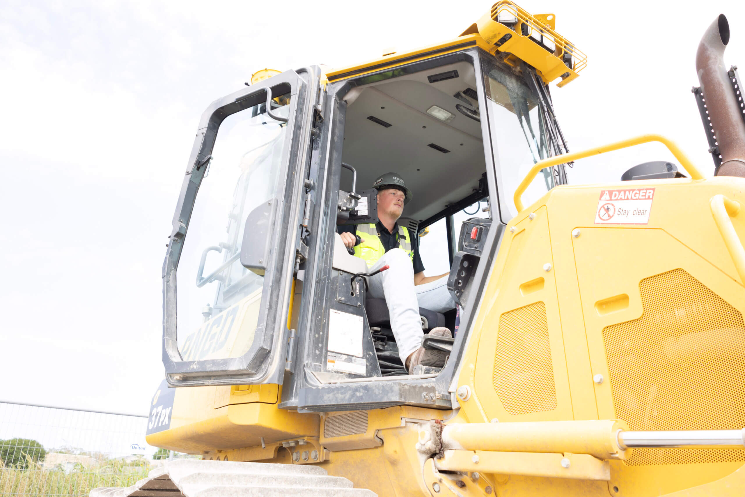 RNGD Project Engineer Makade Penton sits inside heavy construction equipment on an active infrastructure jobsite while wearing PPE and a hard hat.