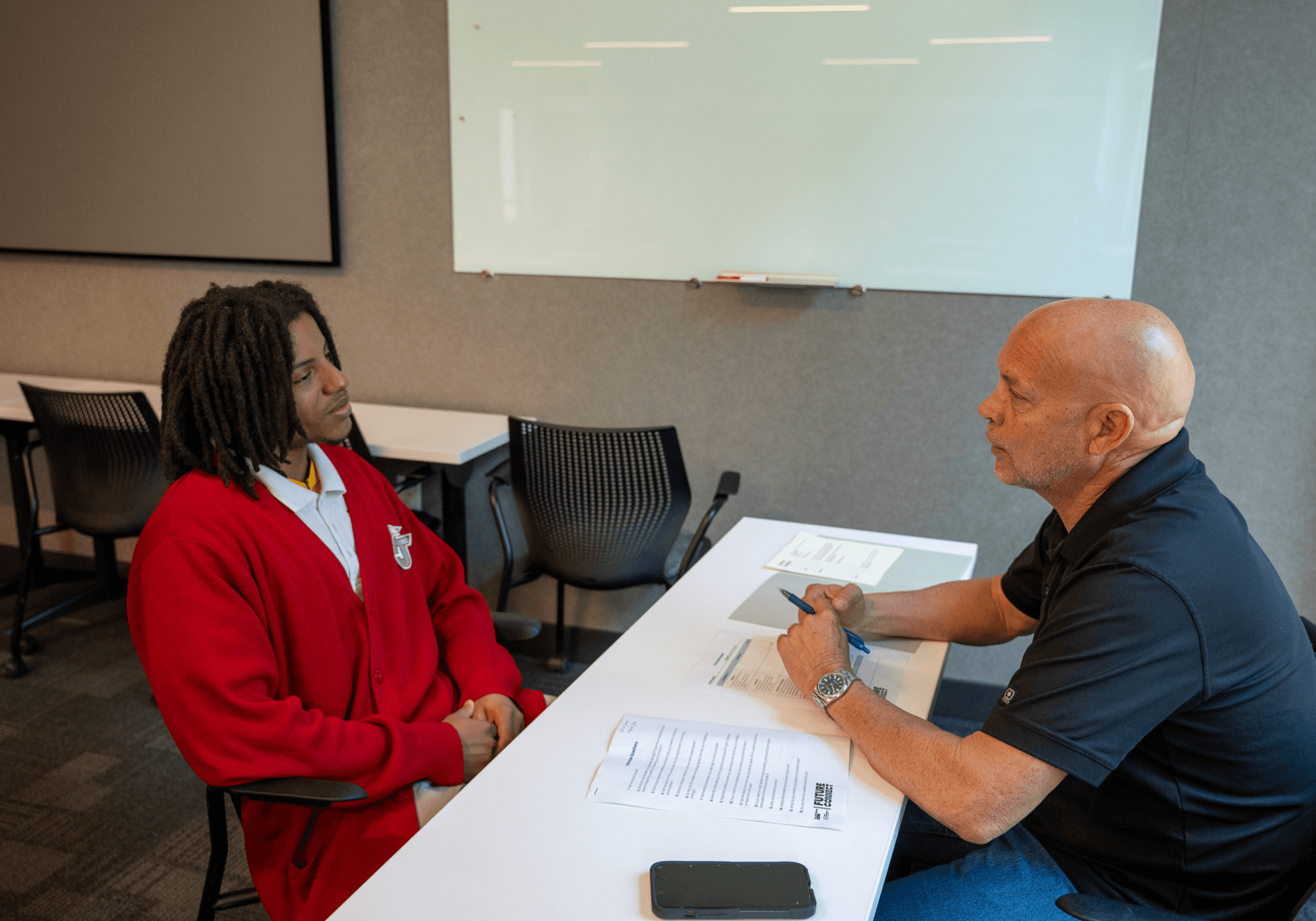 An RNGD team member interviews a student seated across a table in a classroom setting during a career development or mentorship conversation.